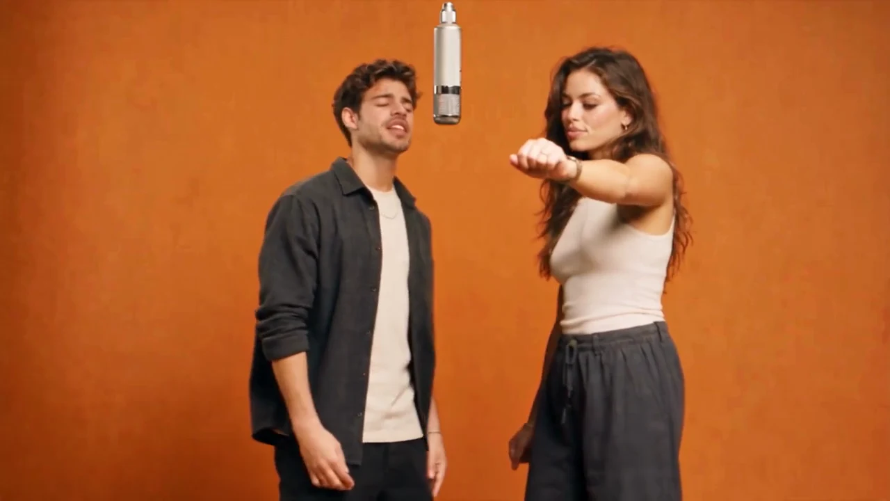 Two performers sharing a hanging microphone in an orange studio